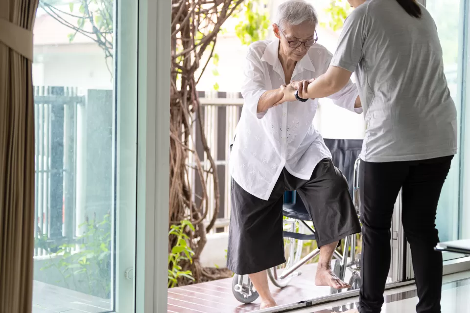 Elderly woman enters house with help from caregiver who is holding her hands